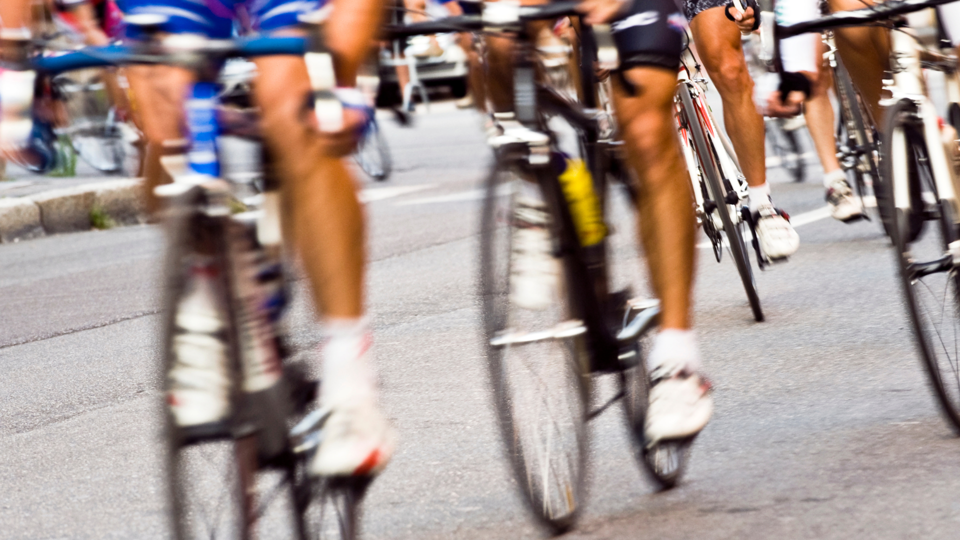 The legs of many cyclists ride their bikes during a city road race.